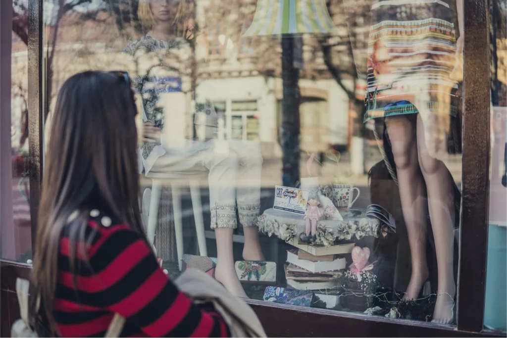Une jeune femme regarde des vêtements au travers d'une vitrine du faubourg de France.